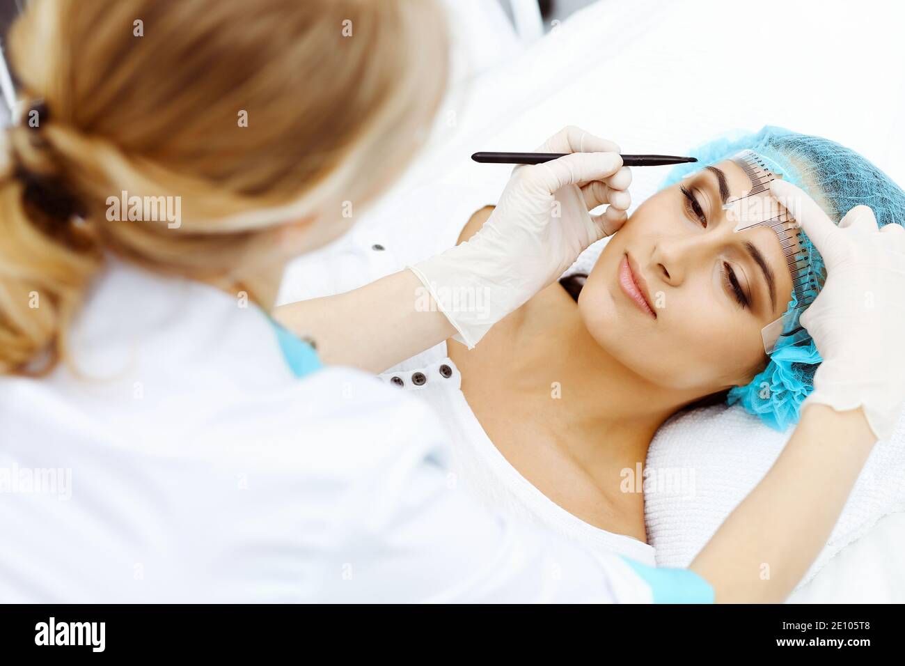 Professional beautician is going to correct eyebrow line at woman face ...