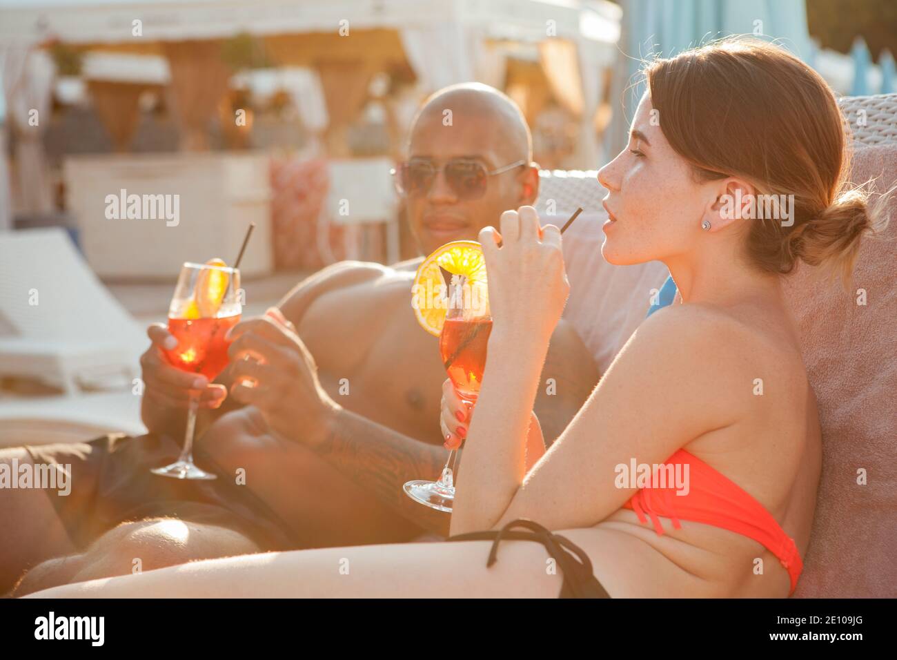 Lovely young woman enjoying drinking cocktail at the beach with her boyfriend. Multiracial couple relaxing at the beach together Stock Photo