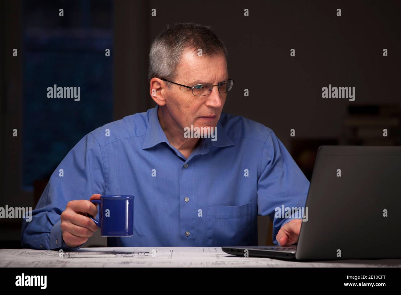 Mature businessman or manager working at home with laptop and a cup of coffee in his hand - dark background Stock Photo