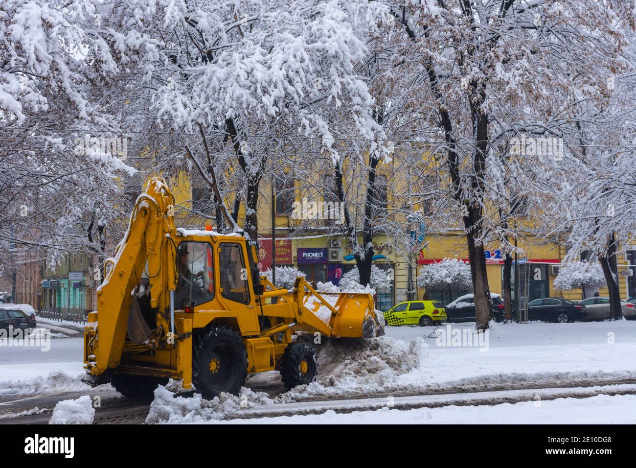 Yellow tractor with snowplow removing snow from the streets. Stock Photo