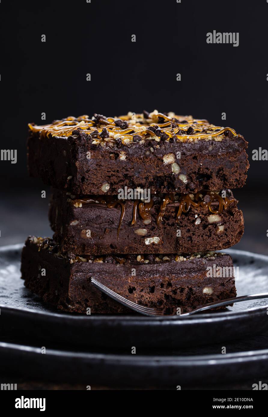 Dark chocolate fudge brownies with caramel and nut topping stacked on a