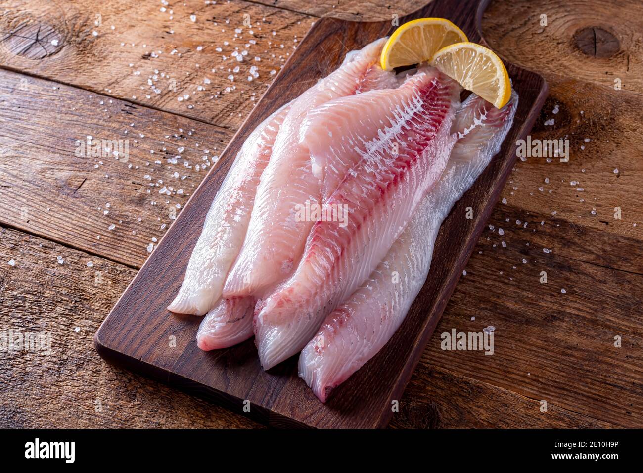 Fresh haddock fillets on a rustic table top with lemon wedges. Stock Photo