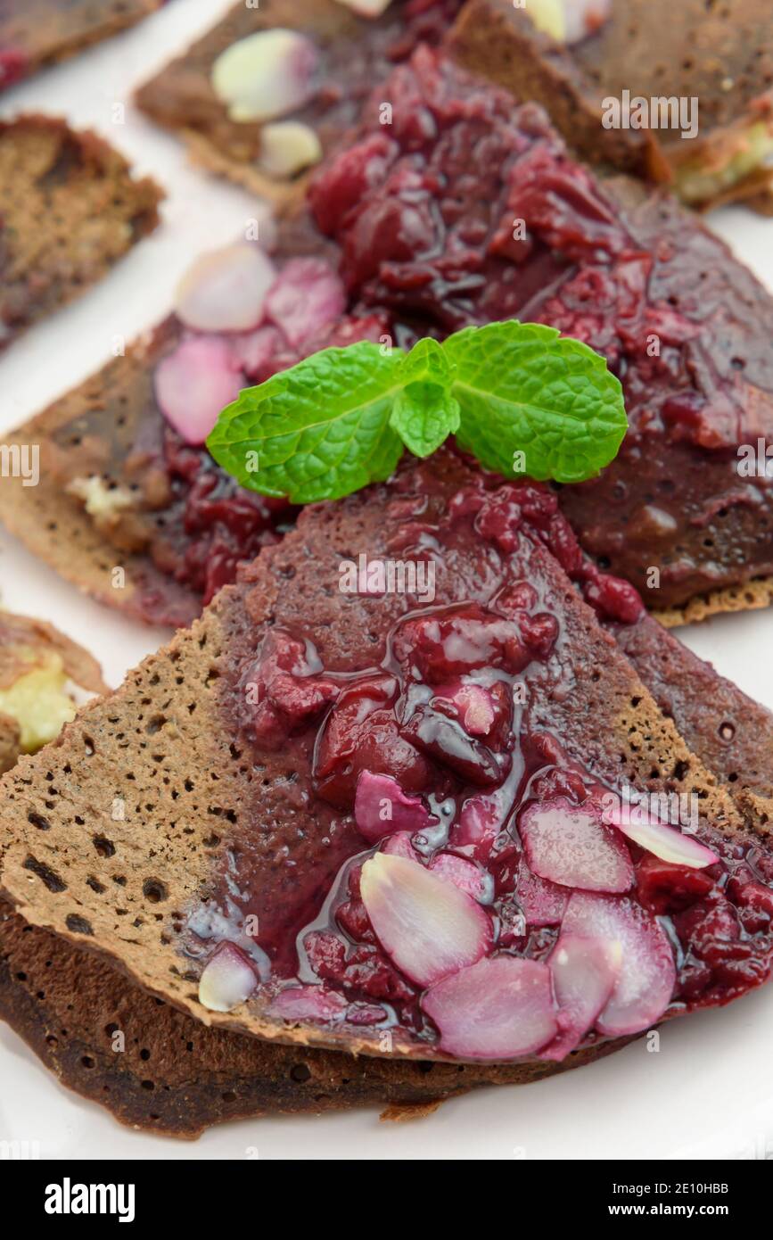 Chocolate vegan, gluten-free french pancakes (crepes) with millet filling and fruit sauce with almonds, 45 degree close-up, happy, bright colors, high Stock Photo