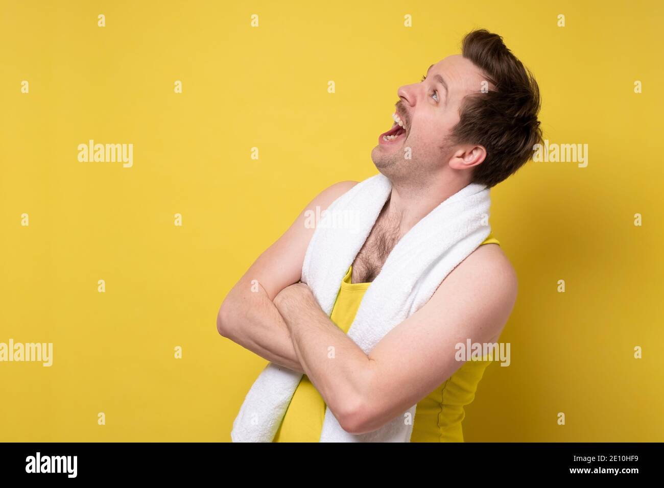 Young caucasian sport man with towel being surprised looking up. Studio shot on yellow wall. Stock Photo