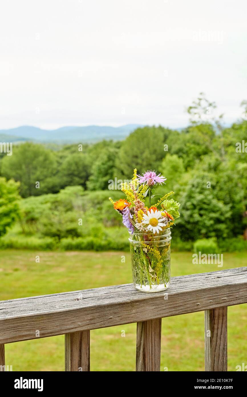 Wildflower Arrangement on a Bare Wooden Railing with Greenery and Sky in the Background, Vertical View 2 Stock Photo