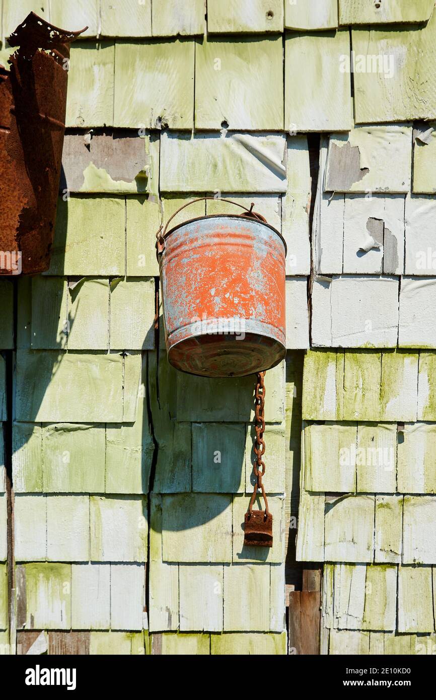 Rusted Grey and Orange Bucket Hanging from Green Wall in Sunlight Stock Photo