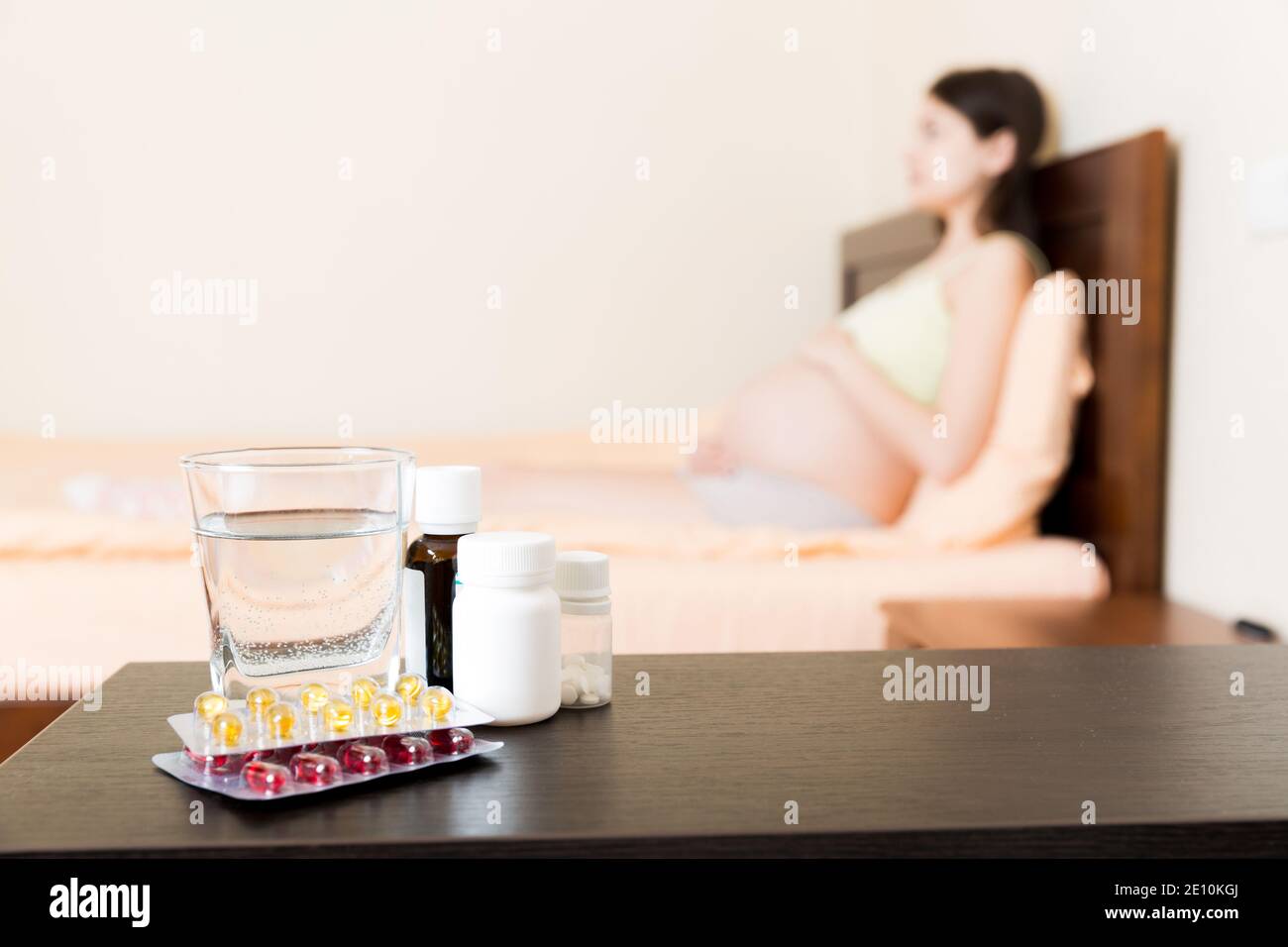 Attractive sick pregnant woman is lying in sofa. Taking pills from colds. Stock Photo