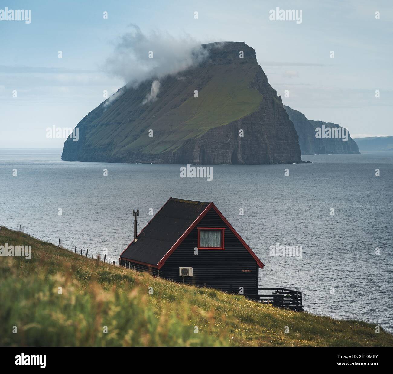 Black house on famous faroese Witches Finger Trail and Koltur island on background. Sandavagur village, Vagar island, Faroe islands, Denmark Stock Photo