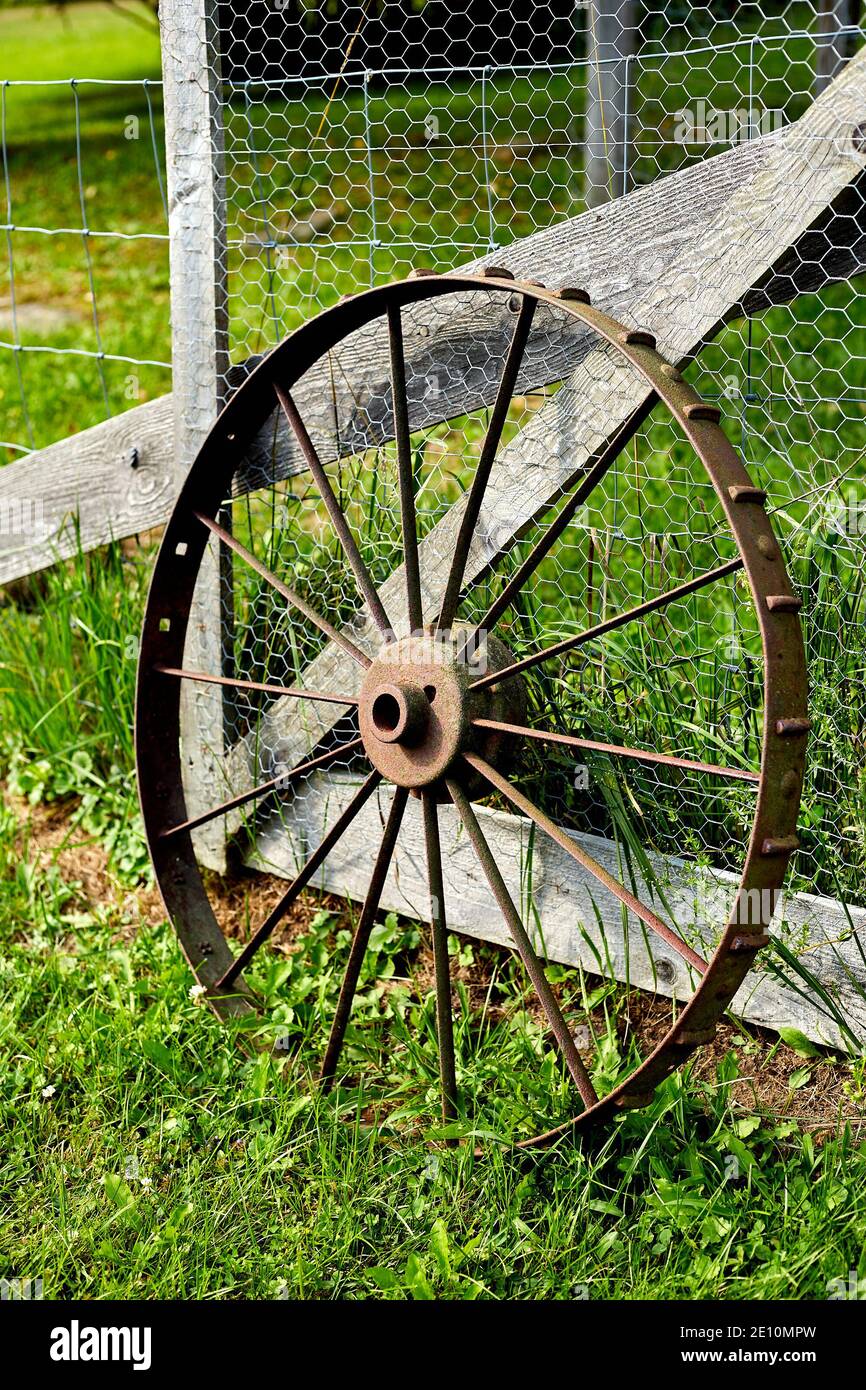 Single Rusty Old Wagon Wheel Leaning on Fence Stock Photo