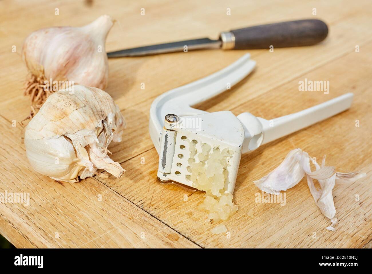 Garlic Bulbs, Knife, and Press on Cutting Board with Freshly Pressed Garlic, Horizontal View 1 Stock Photo