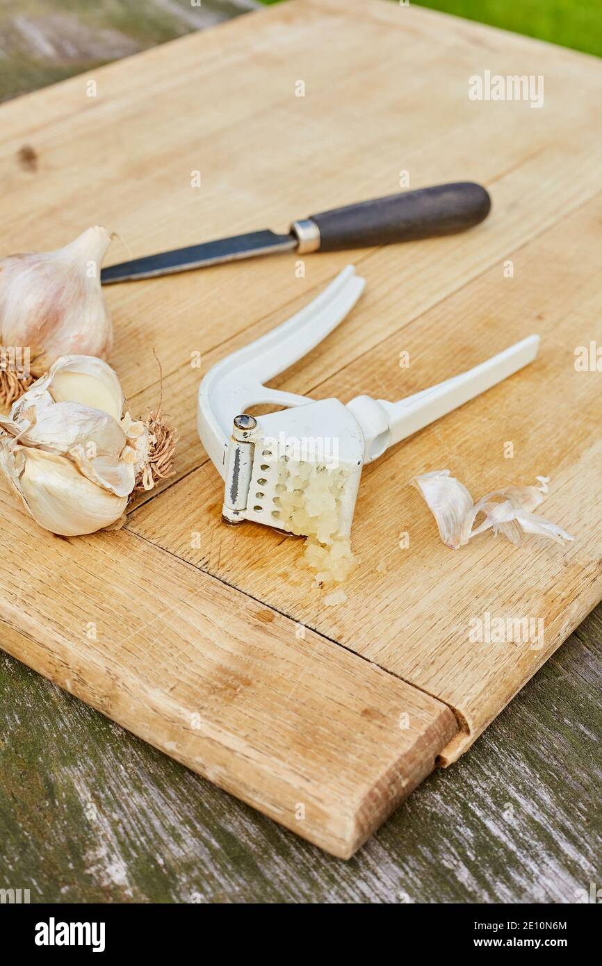 Garlic Bulbs, Knife, and Press on Cutting Board with Freshly Pressed