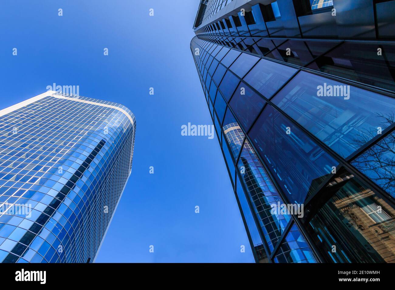 Between two skyscrapers. Looking up at buildings in Frankfurt. blue window front from the skyscraper in sunshine and blue sky. Commercial buildings in Stock Photo