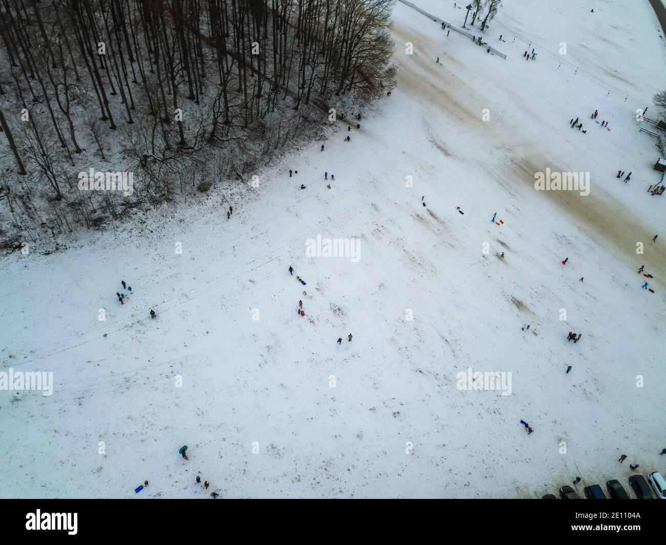 Aerial view of people enjoying a winter day by sledding on a small ski slope during winter holidays. The ski lift is not operating due to the Corona Stock Photo