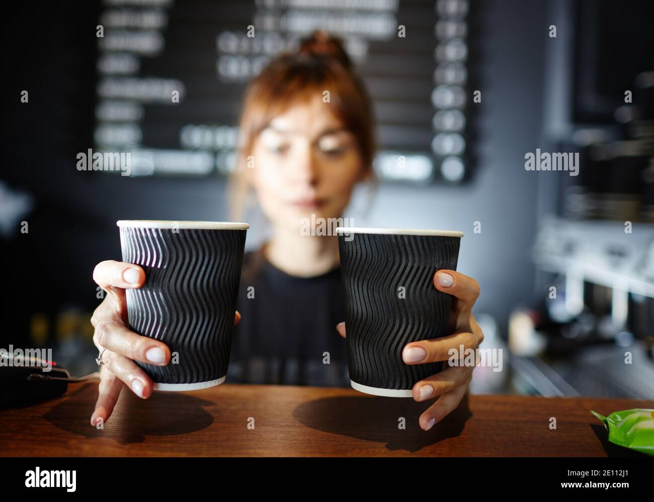 Barista holds two disposable paper cups of coffee in coffee shop. Blurred image, selective focus Stock Photo