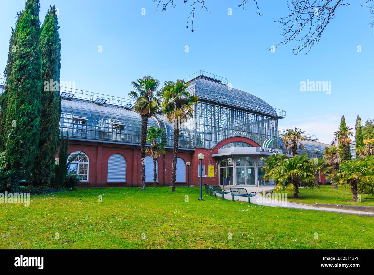 Buildings of palm garden in Frankfurt. Palm trees and cypresses with a meadow in front of the entrance. Glass roof with windows and bricks from the bu Stock Photo