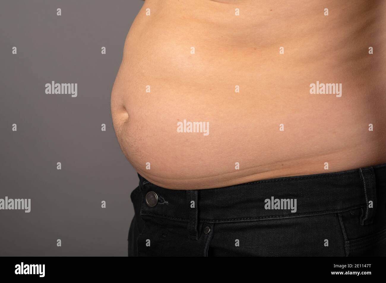 Close up picture of young man's bloated stomach in front of grey background Stock Photo