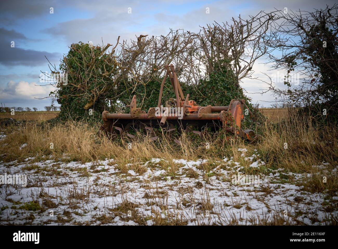 Old Howard agricultural PTO driven rotovator abandoned at the edge of a  field by a hedgerow in the snow Stock Photo