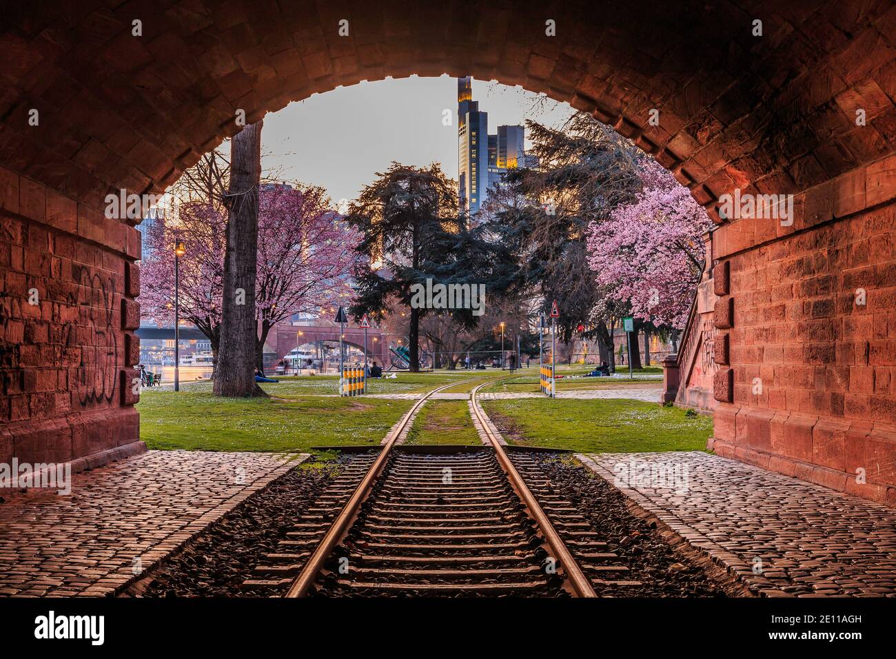 Railway tunnel with an old track through a park on the banks of the Main. Frankfurt skyline with skyscrapers in the background in the evening. Violet Stock Photo