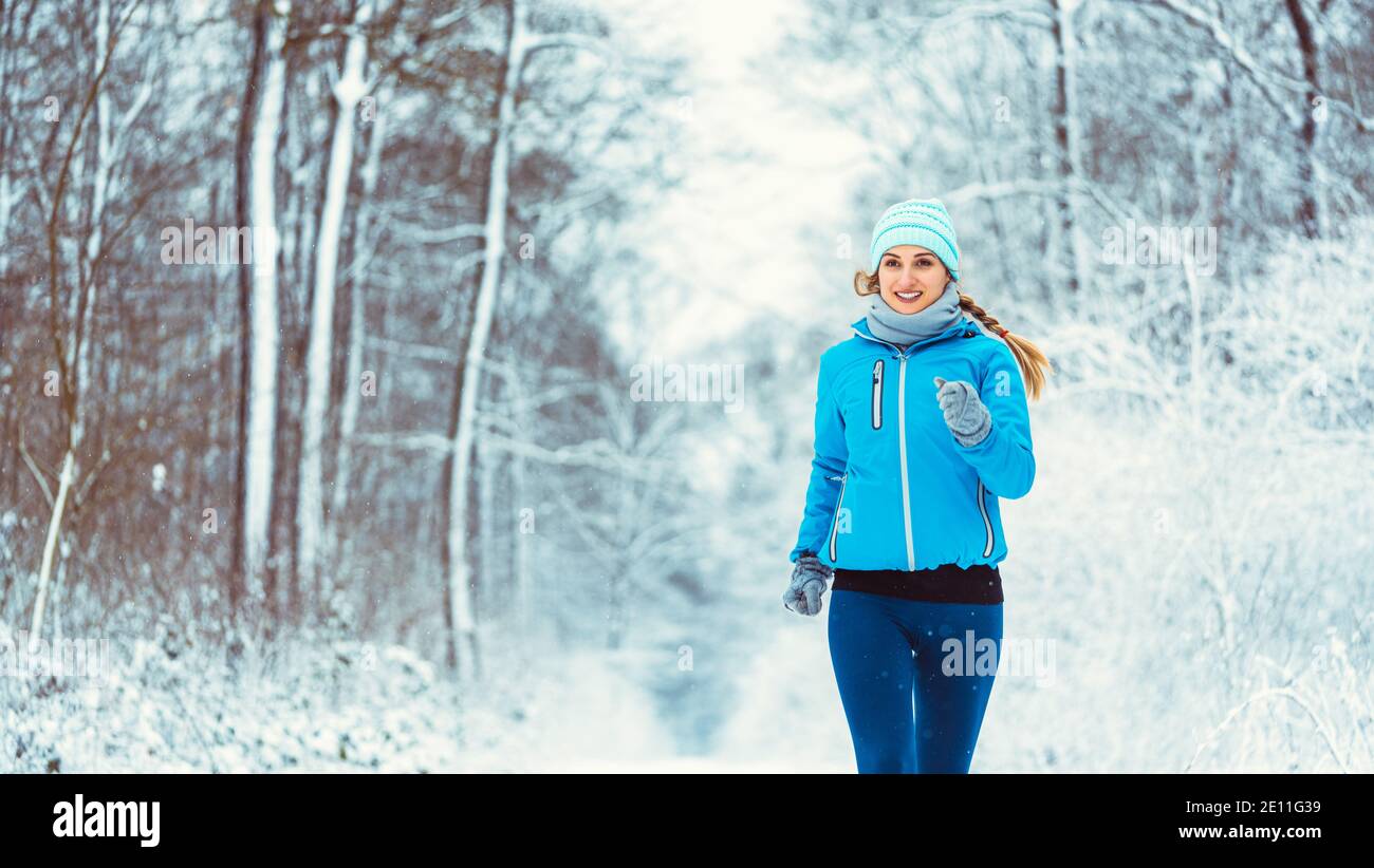 Woman jogging towards camera in cold and snowy forest Stock Photo