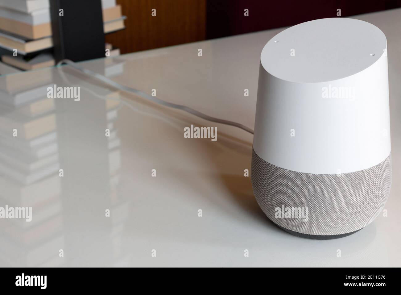 white voice activated virtual assistant, smart speaker on a home desk with a stack of books in the background reflecting on the desk, with copy space Stock Photo