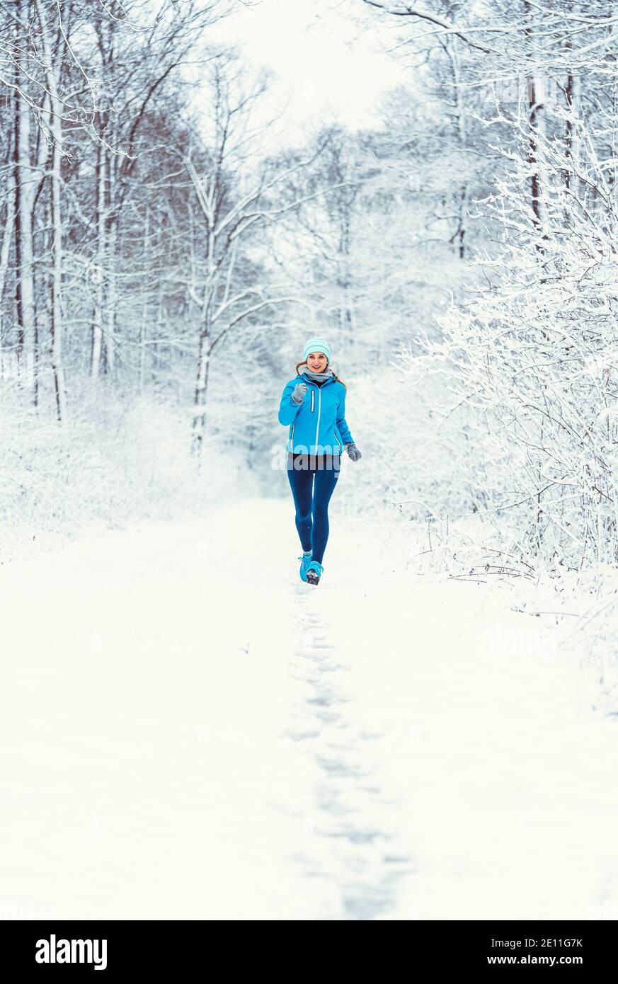 Woman jogging towards camera in cold and snowy forest Stock Photo