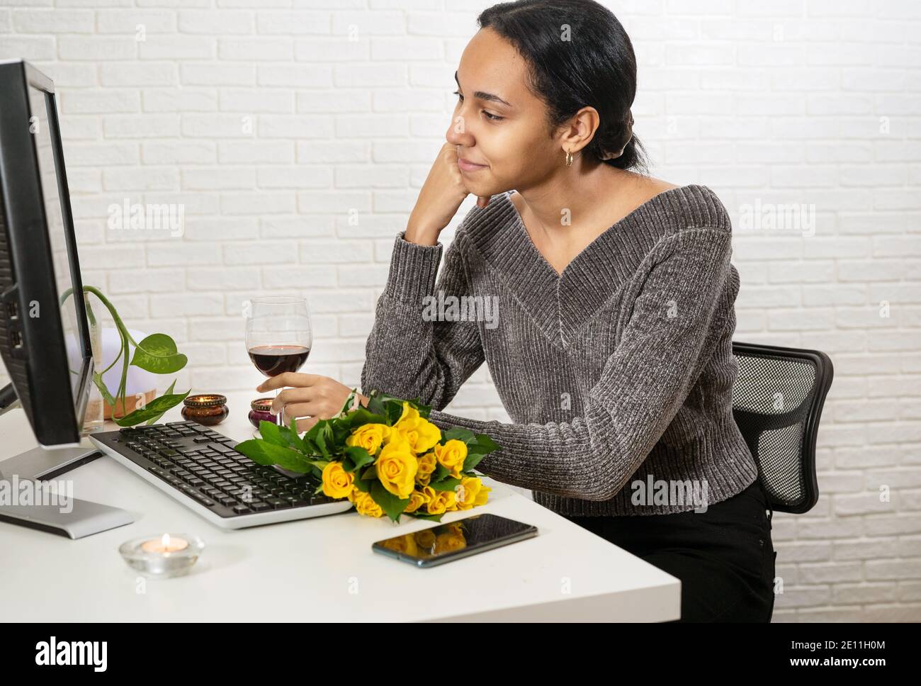 Young pretty mixed-raced woman speaking with someone online in romantic atmosphere Stock Photo