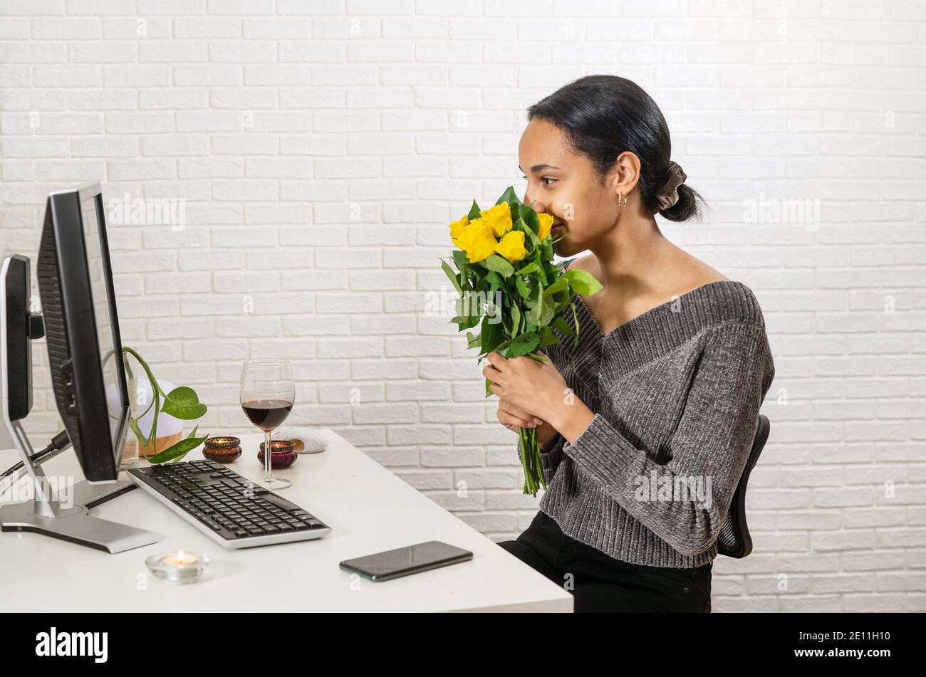 Young pretty mixed-raced woman holds a bunch of yellow roses in front of her face and speaking online Stock Photo