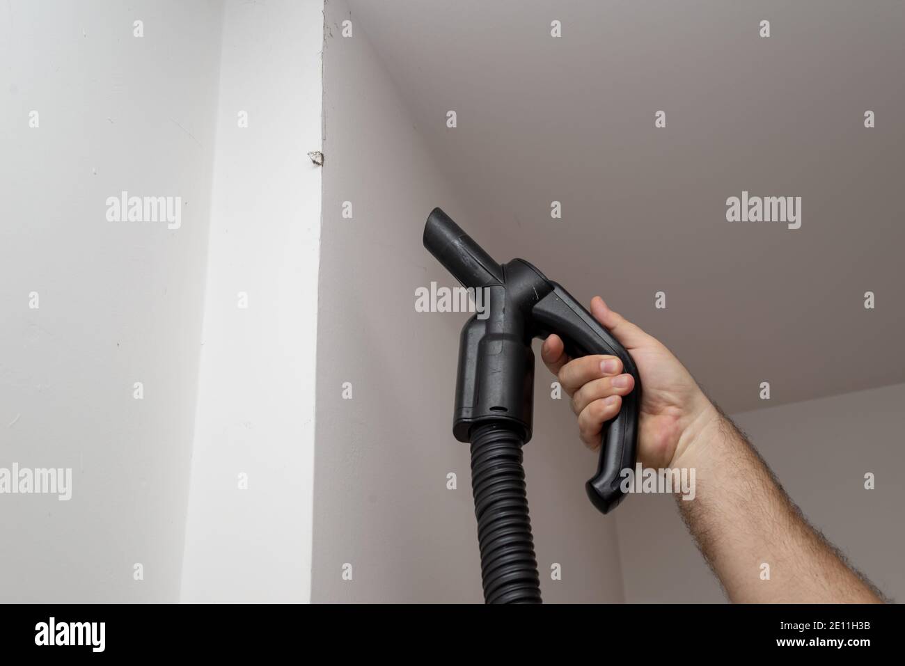 Hand of a man holding a vacuum cleaner while vacuuming dirt on a wall