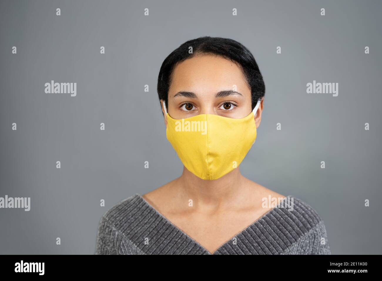 Young pretty mixed-raced woman portrait wearing yellow mask and staying against gray background Stock Photo