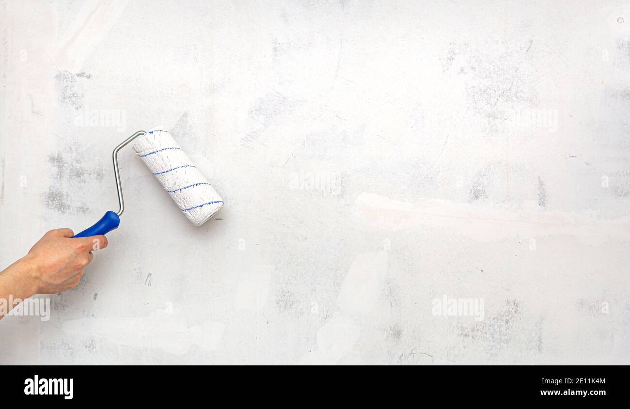 Hand with paint roller on background of empty concrete white wall. Repair. Stock Photo