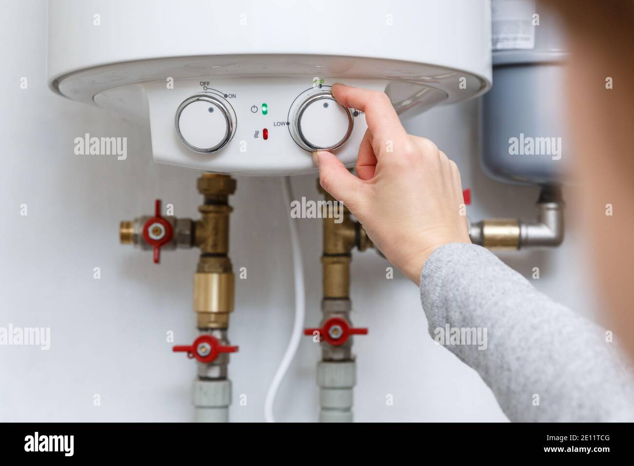 Female hand puts thermostat of electric water heater (boiler) in economy mode. Household enegry saving equipment Stock Photo