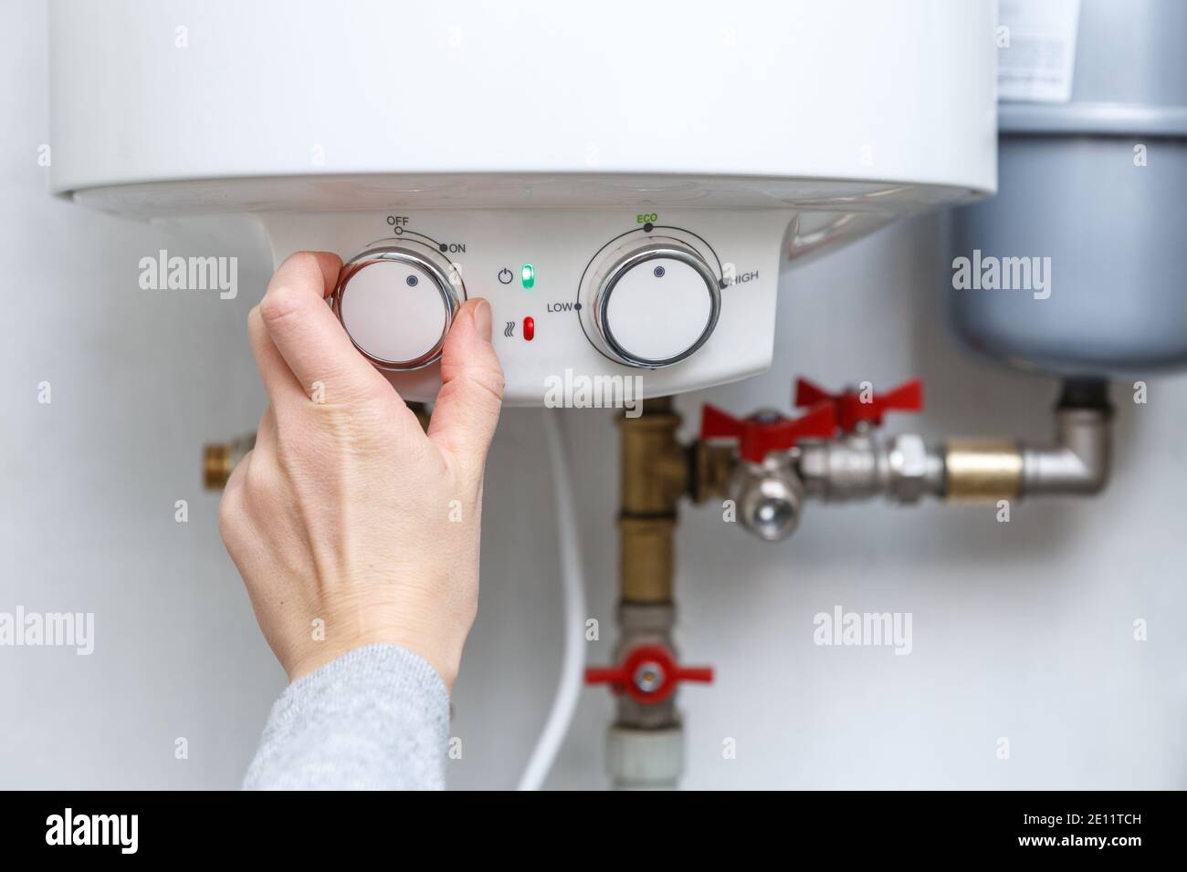 Female hand turning on electric water heater (boiler). Household enegry saving equipment Stock Photo