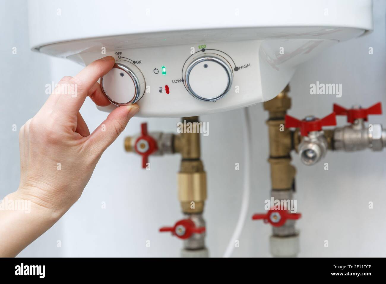 Female hand turning on electric water heater (boiler). Household enegry saving equipment Stock Photo