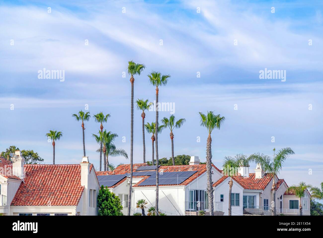 Red tile roofs of homes with solar panels against cloudy blue sky and ...