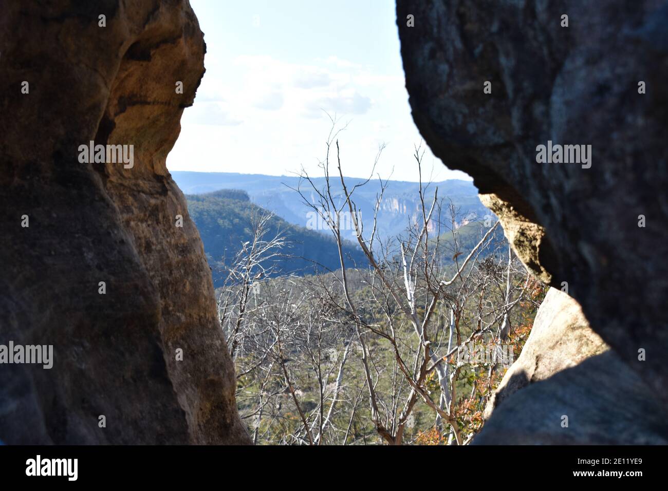 a hole in a cliff face on a mountain with blue mountain views in the background Stock Photo