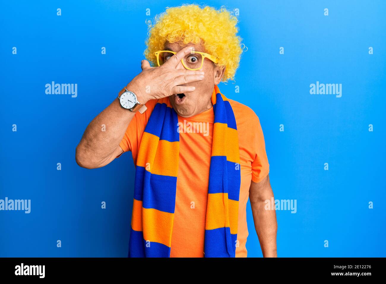 Senior hispanic man football hooligan cheering game peeking in shock ...