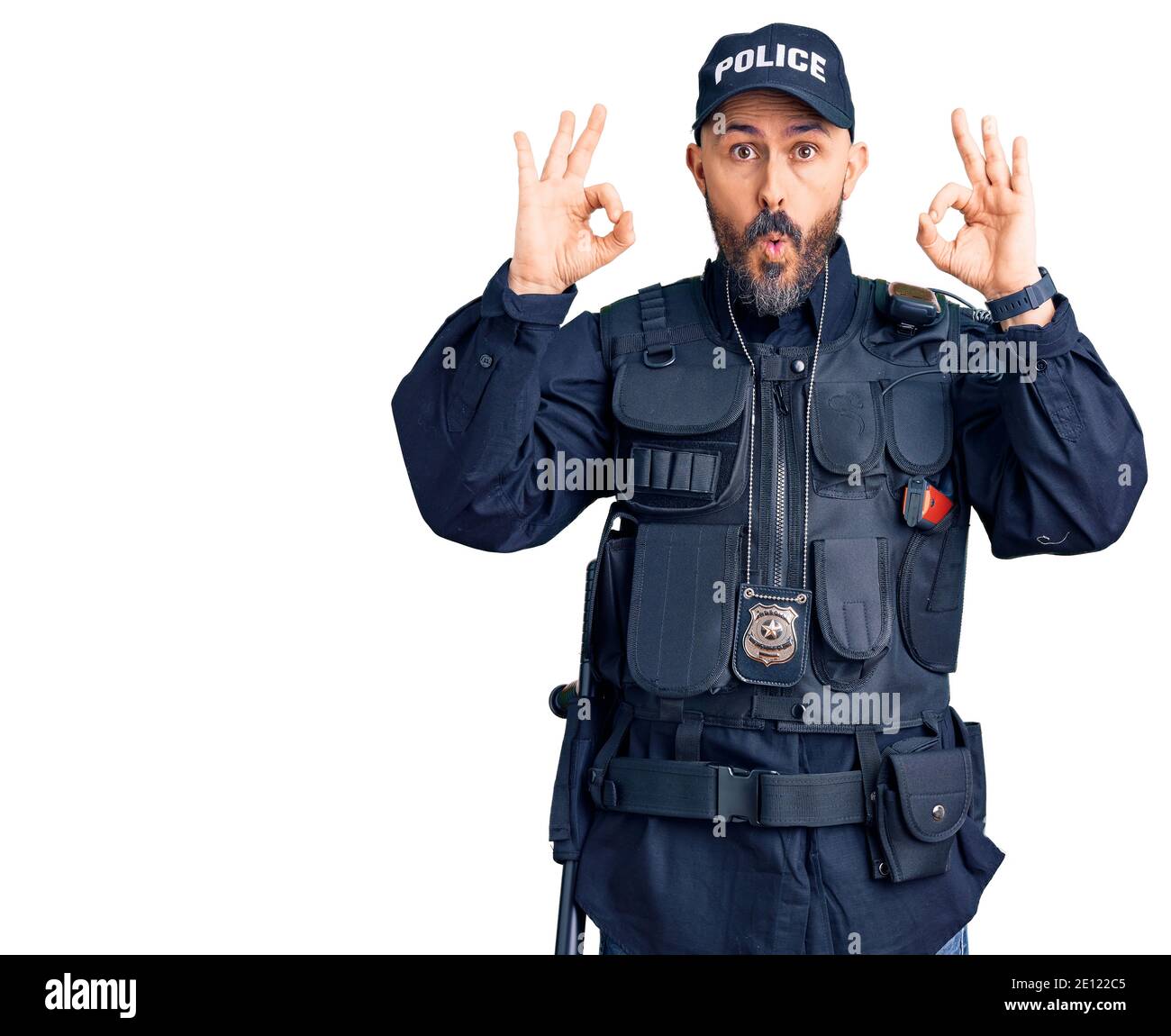 Young handsome man wearing police uniform looking surprised and shocked doing ok approval symbol with fingers. crazy expression Stock Photo