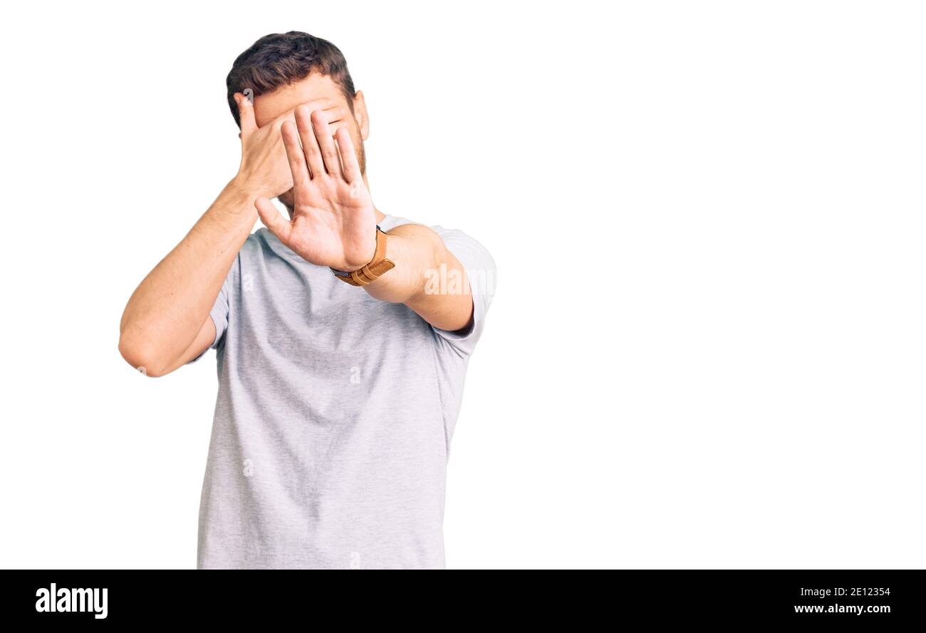 Handsome young man with bear wearing casual tshirt covering eyes with hands and doing stop gesture with sad and fear expression. embarrassed and negat Stock Photo