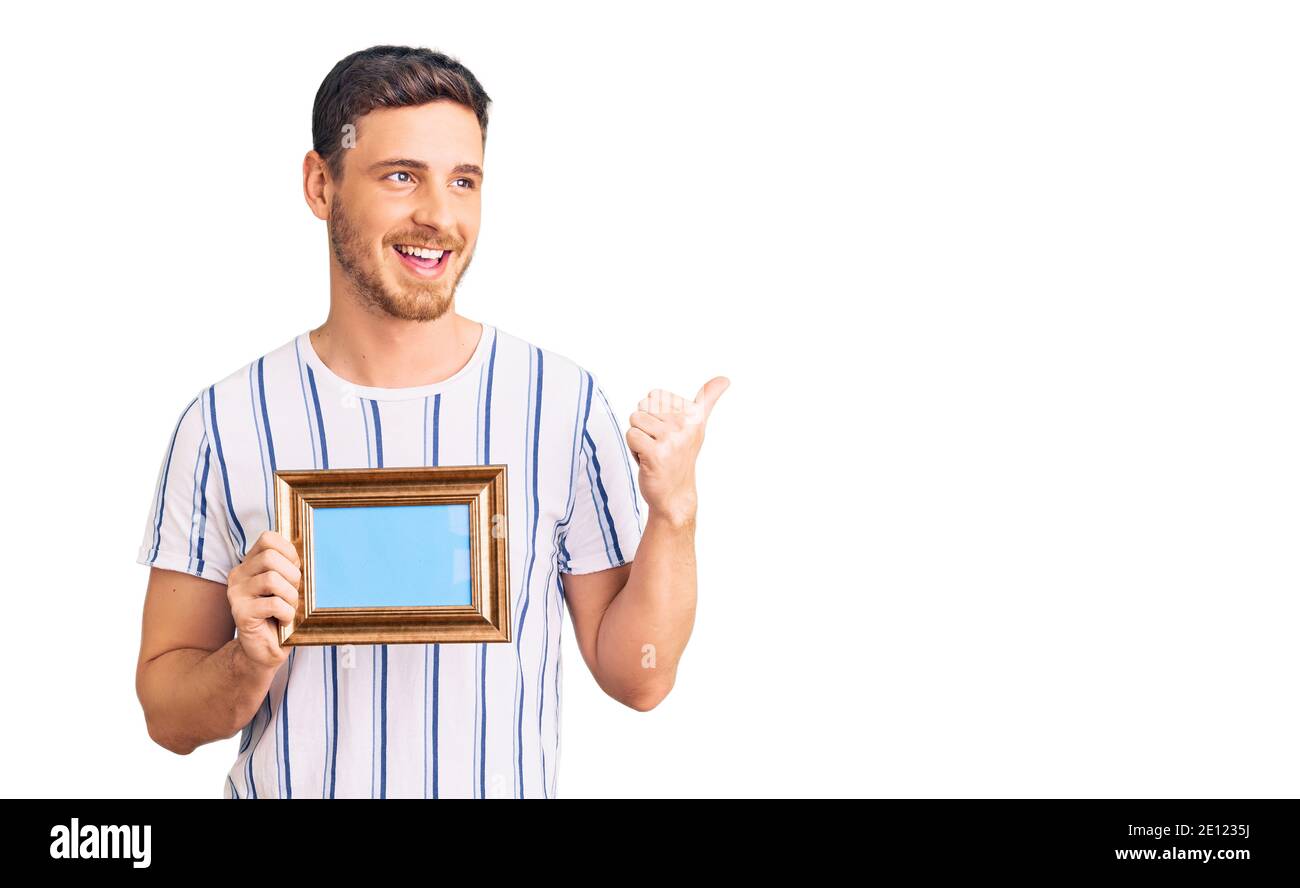 Handsome young man with bear holding empty frame pointing thumb up to ...