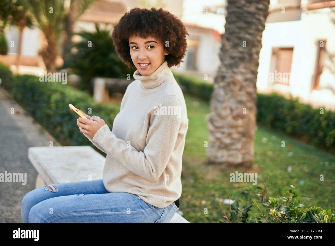 Young hispanic girl smiling happy using smartphone sitting on the bench ...