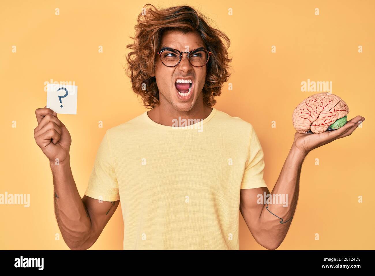 Young hispanic man holding brain and question mark angry and mad ...