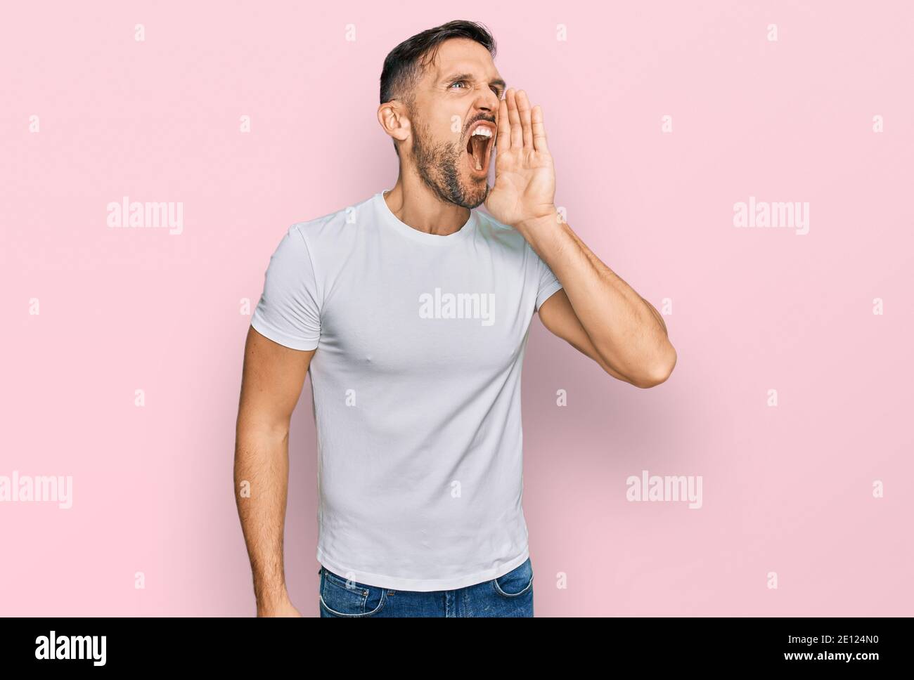 Handsome man with beard wearing casual white t shirt shouting and ...