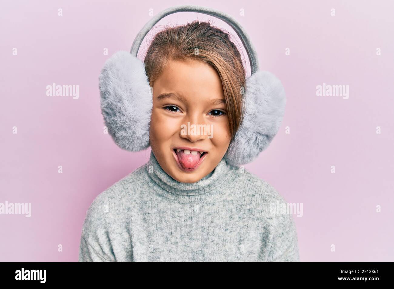 Little beautiful girl wearing fluffy earmuff sticking tongue out happy