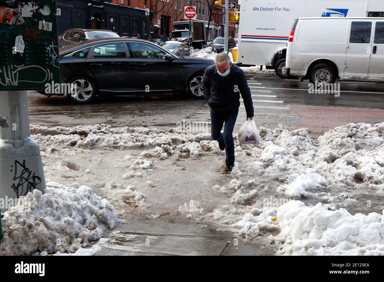 A person stumbles into ankle-deep dirty slush water at a crosswalk resulting from melting snow and clogged sewers in New York City Stock Photo