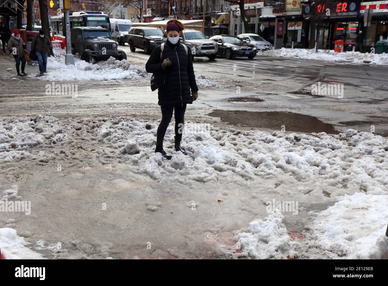 A person contemplates how to cross an ankle-deep puddle of dirty slush water at a crosswalk in New York, NY. Stock Photo