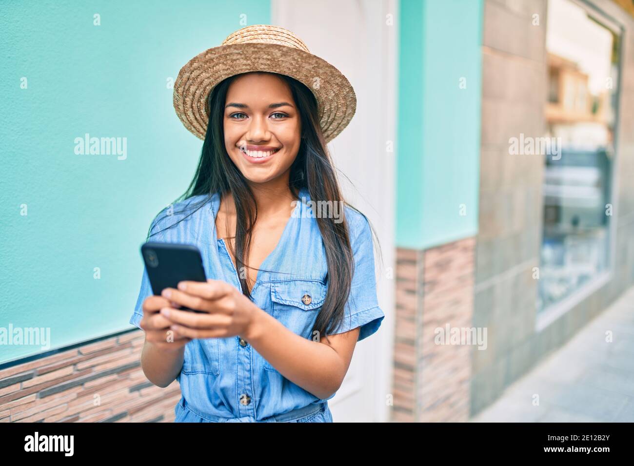 Young latin tourist girl on vacation smiling happy using smartphone at ...