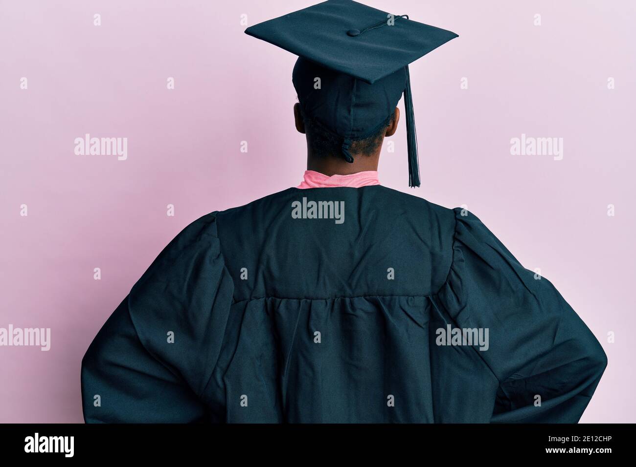 Young african american girl wearing graduation cap and ceremony robe standing backwards looking away with arms on body Stock Photo