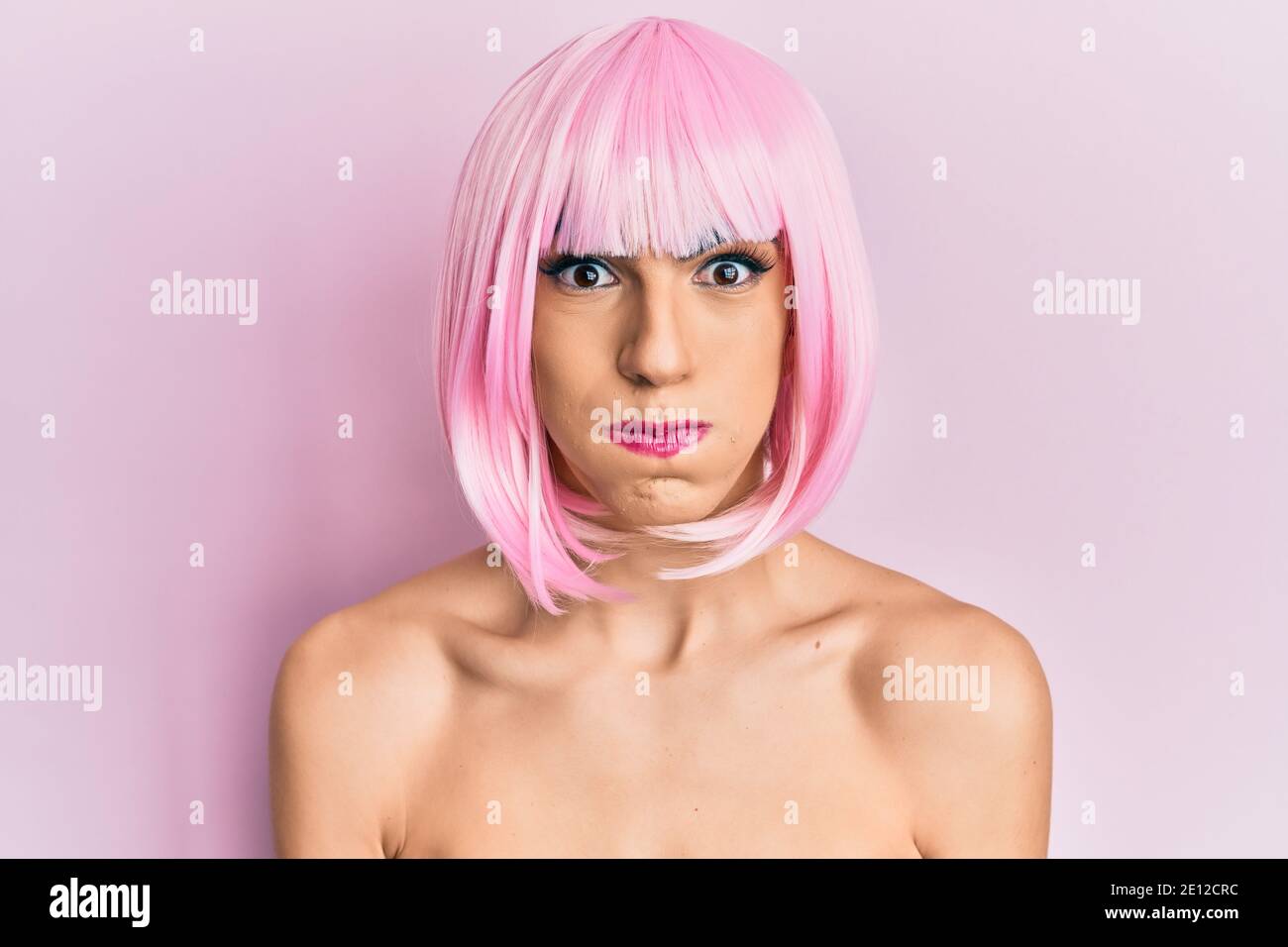 Young man wearing woman make up wearing pink wig puffing cheeks with funny face. mouth inflated with air, crazy expression. Stock Photo