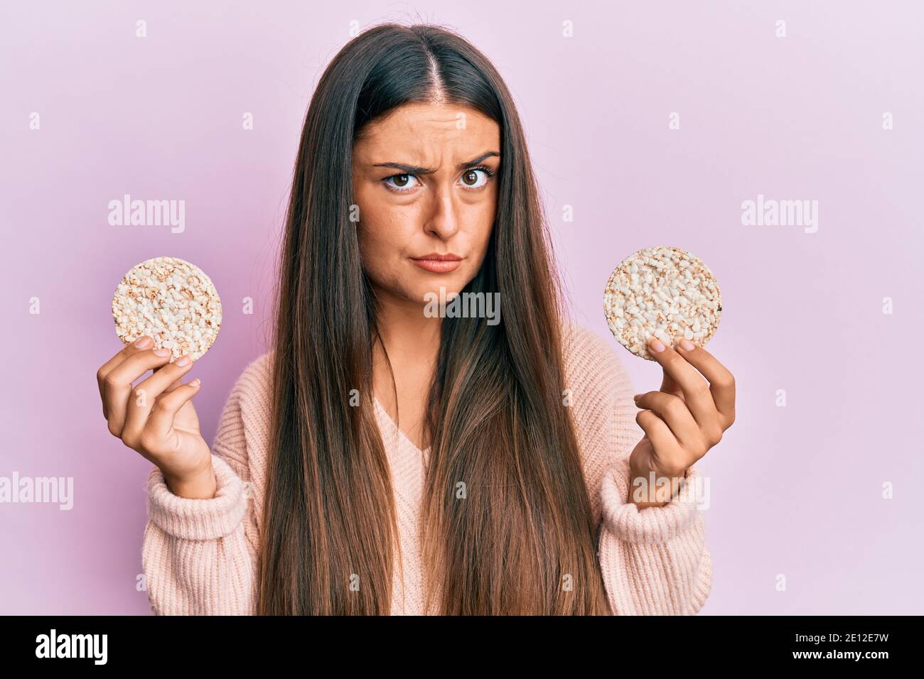 Beautiful hispanic woman eating healthy rice crackers skeptic and