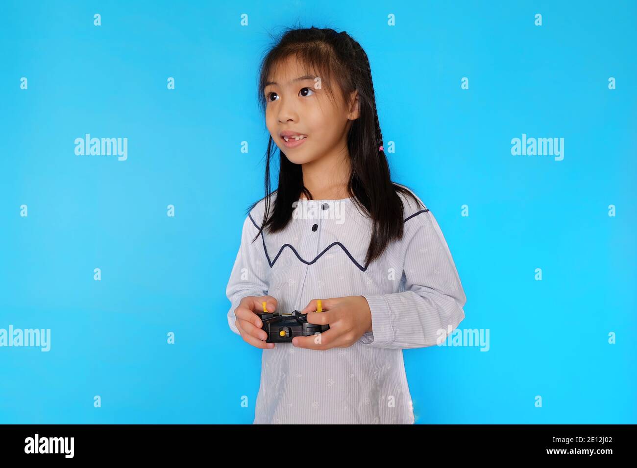 A cute Asian girl is playing with her drone, controlling it though her radio transmitter. Plain light blue background. Stock Photo